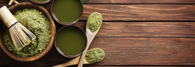 An assortment of matcha powder, stir stick, matcha powder on spoons and matcha in cups on a wooden table
