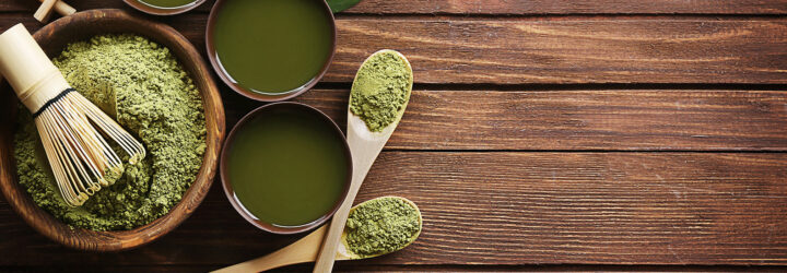 An assortment of matcha powder, stir stick, matcha powder on spoons and matcha in cups on a wooden table