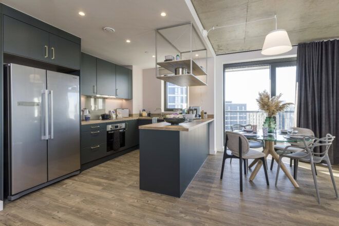 Kitchen with dark green cabinetry and dining space with rattan furniture in modern apartment