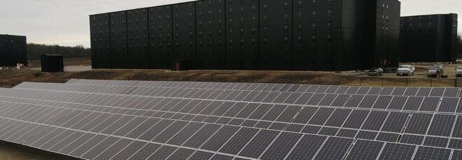 Rows of solar panels in front of a black distillery building
