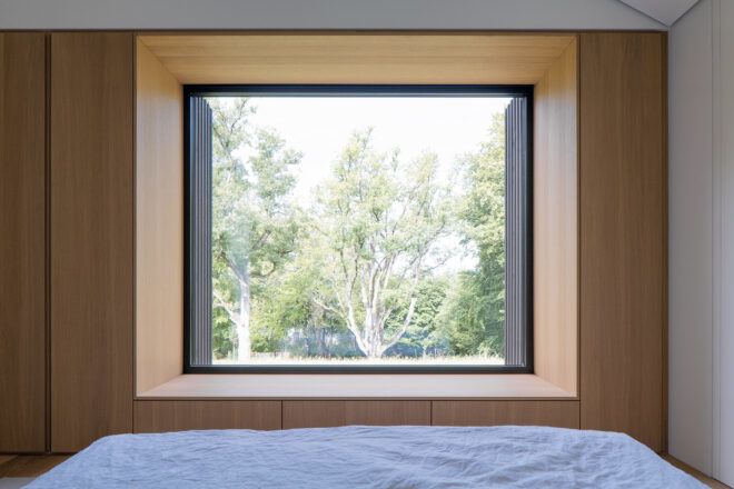 A large window of a bedroom looking out to a forest