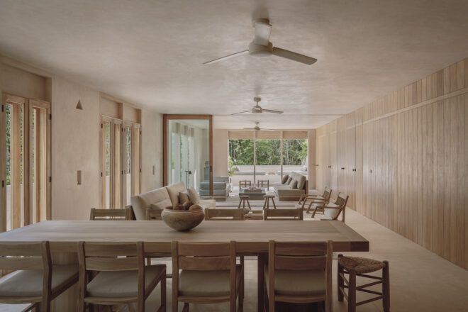 A dining and living room space in cream tones with ceiling fans and large windows