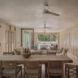 A dining and living room space in cream tones with ceiling fans and large windows