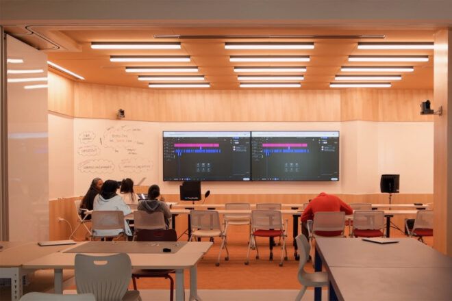Students seated at one long table with two large screens on the wall at the back