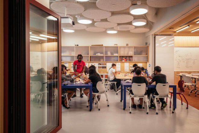 Open plan classroom where students are seated and collaborating at three tables