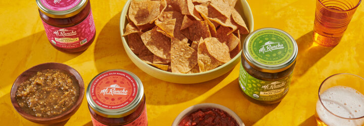 A basket of tortilla chips, jars of salsa and a bowl of green salsa