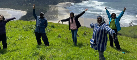 A group of five people posing on a hill side overlooking an ocean