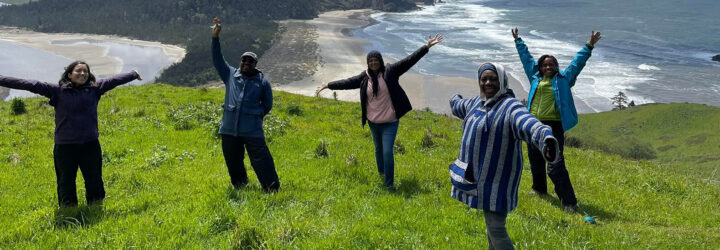 A group of five people posing on a hill side overlooking an ocean