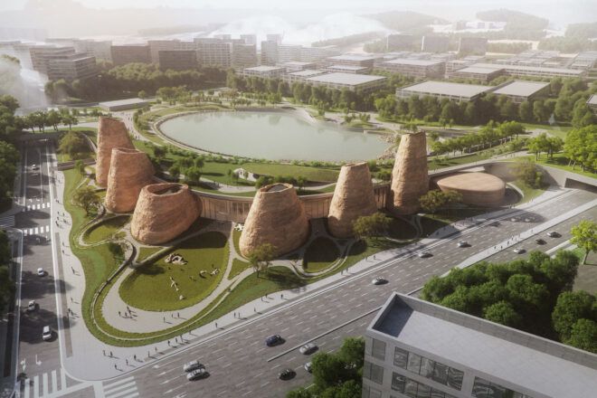 Aerial view of a curving building flanked by earthy cone-like forms, facing a large water body