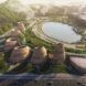Aerial view of a curving building flanked by earthy cone-like forms, facing a large water body