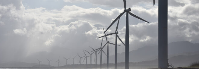 Wind turbines lined up in a row beside a coastline