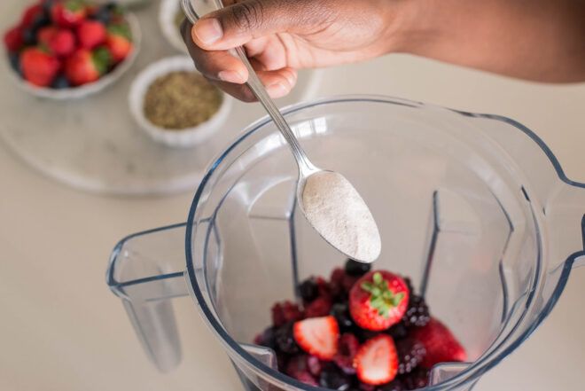 A spoon scooping a white powder into a blender of berries