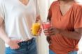 Two people holding an orange and pink glasses of smoothies