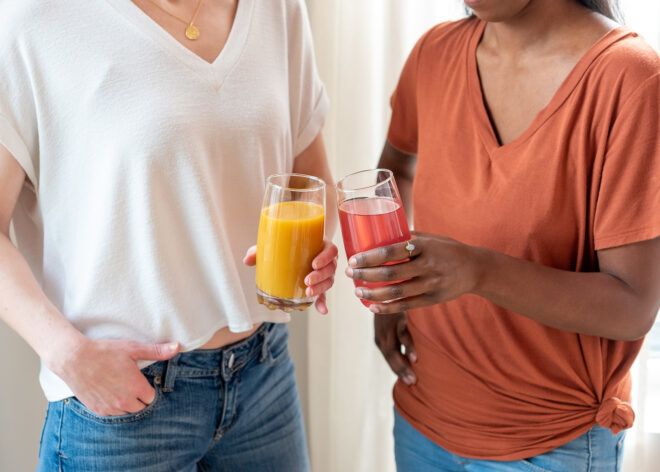 Two people holding an orange and pink glasses of smoothies
