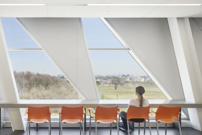 A table facing a window with a person sitting on one of the many orange chairs