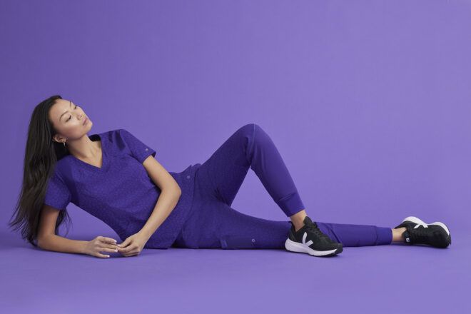 A woman dressed in purple scrubs in front of a purple background
