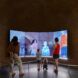 Three children and two adults watching themselves through a pixelated screen