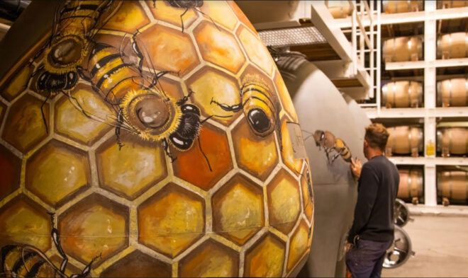 A man painting honeycomb and bees on the exterior of a gray surface