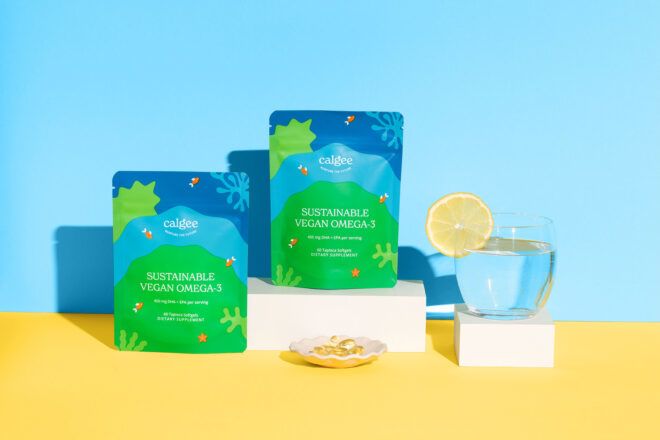 Two bags of Calgee Omega-3 and a glass of water with a lemon wedge on the lip