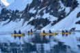 Multiple people floating in a river by a snowy mountain in yellow kayaks