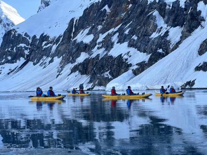 Multiple people floating in a river by a snowy mountain in yellow kayaks