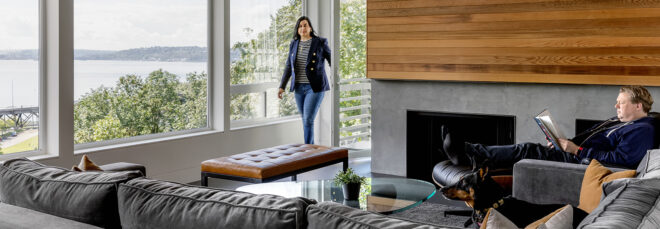 A living room space with a wood wall decor above the fireplace and a wall of windows on the left