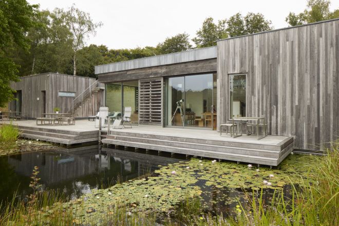A wooden home with a lake in the front yard and glass windows