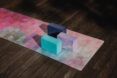 Three cubes (blue, purple and dark blue) on a pink mat