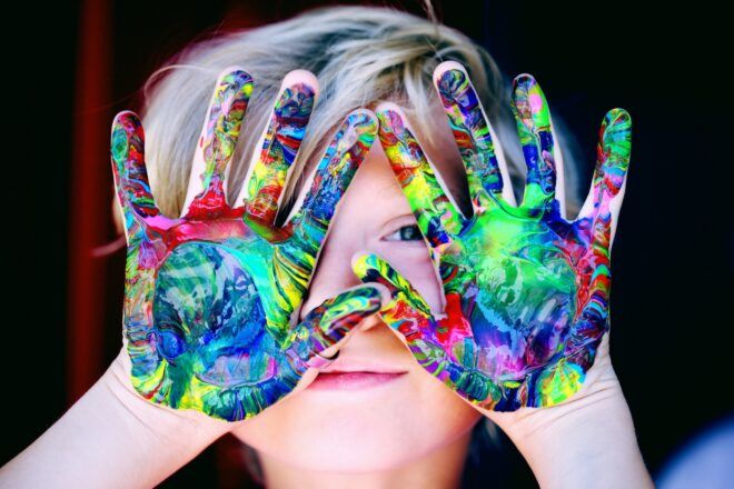 A child covering their face with their hands stained with paint
