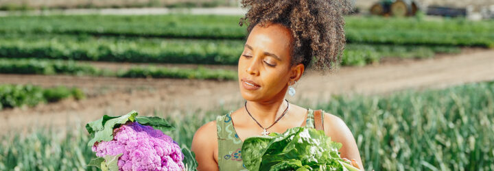 A dark-skinned person holding a purple cauliflower and cabbage in either of their hands