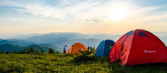 A row of three tents perched on a hill overlooking a mountain range