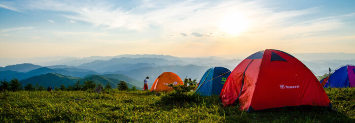 A row of three tents perched on a hill overlooking a mountain range