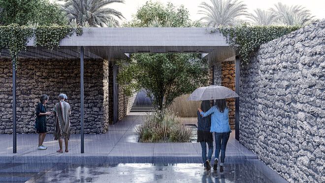 Two people huddled underneath an umbrella beside a wall and an open walkway