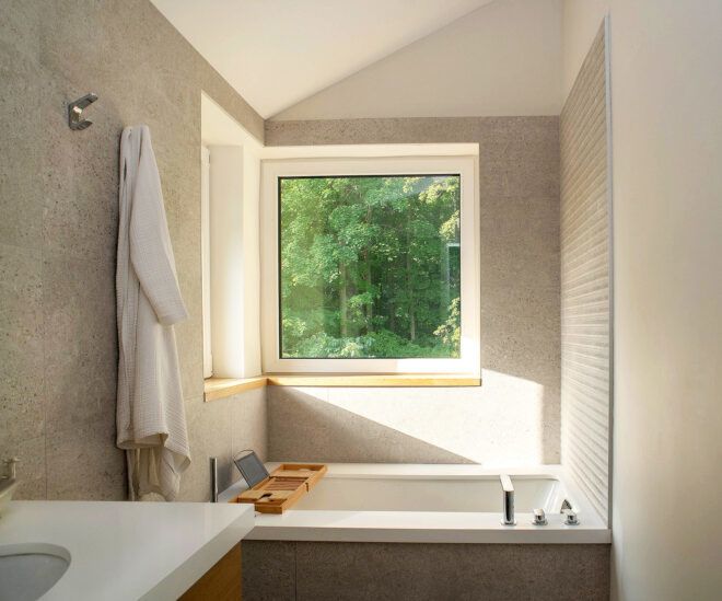 A bathroom with an open square window behind the bathtub