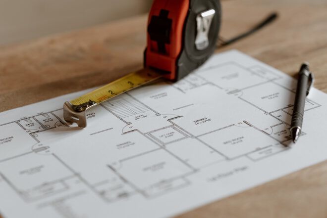 A measuring tape with a white paper with a layout of a building and a pen on top of it