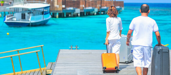 A couple rolling their suitcases toward a bridge at the end of a pier