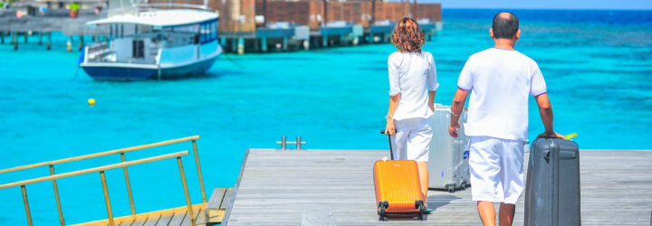A couple rolling their suitcases toward a bridge at the end of a pier