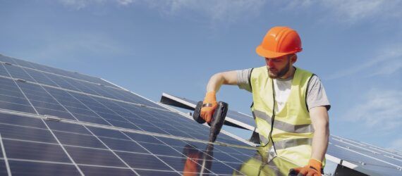 A man wearing a safety vest and hard hat installing a solar panel