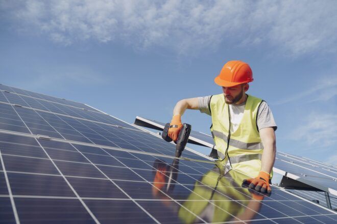 A man wearing a safety vest and hard hat installing a solar panel