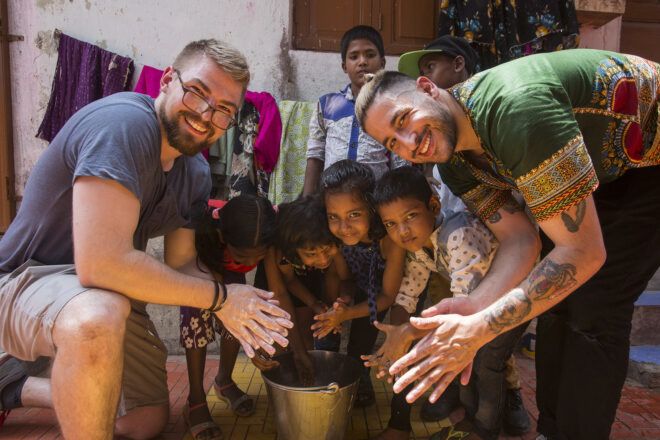 A group photo with two men and a group of children huddled over a bucket of water